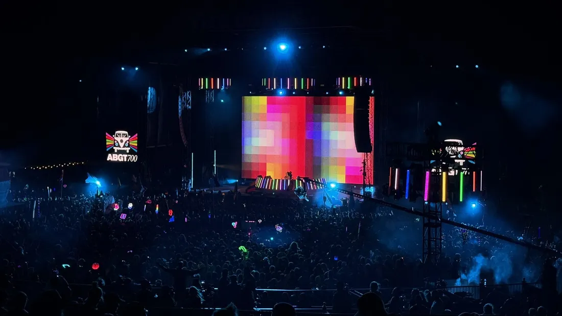 The ABGT700 mainstage at the Gorge after dark, a wall of coloured squares lit behind the booth, the ABGT700 camper van logo on the side screen, and the crowd below it, full to the rail and holding lit totems, seen from up the hill.