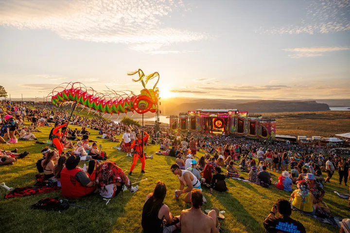 The Gorge at sunset: the crowd spread across the grass slope above a stage, the Columbia River canyon and the far cliffs behind it.