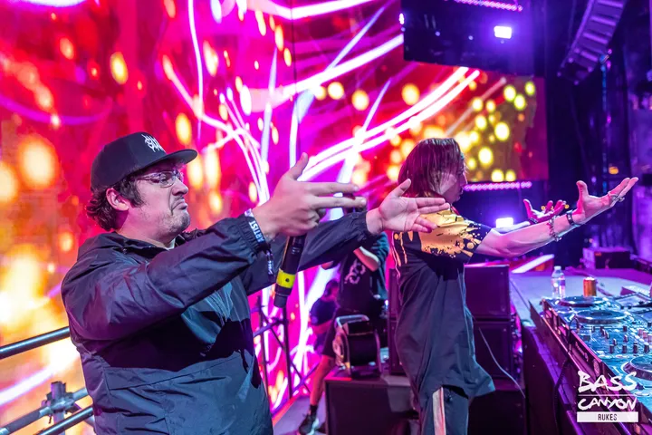 Two performers at the front of the deck throwing their arms out, magenta and orange lasers filling the screen behind them.