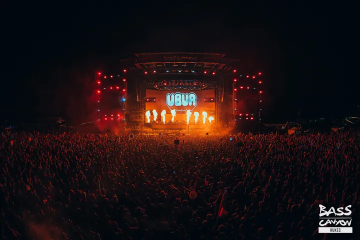 The Paradox stage at night from the back of the crowd, the LED wall lit red above a dense silhouetted field of people.