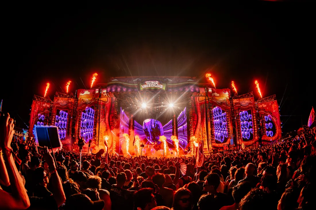 The Beyond Wonderland main stage at the Gorge after dark, flame jets firing along the top of a red and purple proscenium, the crowd silhouetted in front of it.